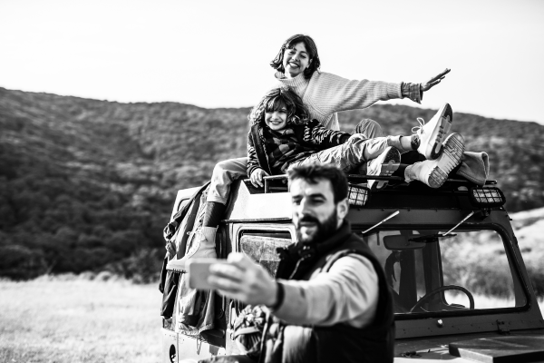 Image of a family with 2 people sitting on a campervan and a man taking a picture
